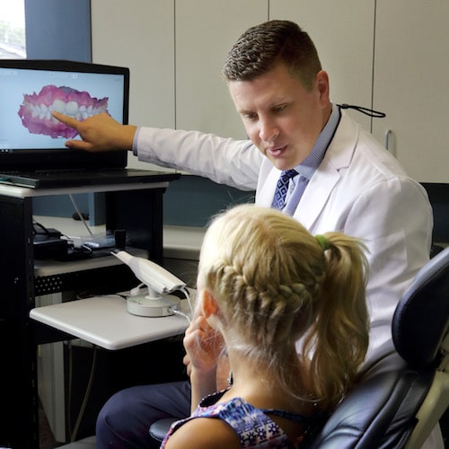 Dr. Vetter, your family dentist in Fargo, pointing at a monitor while speaking with a young patient