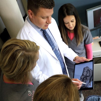 Your family dentist in Fargo, Dr. Vetter, and his team standing and looking at the iPad with images on it. 