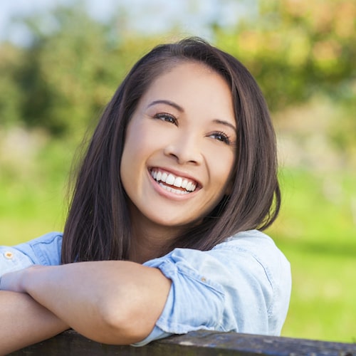 Woman leaning on a wooden gate, looking up, and smiling